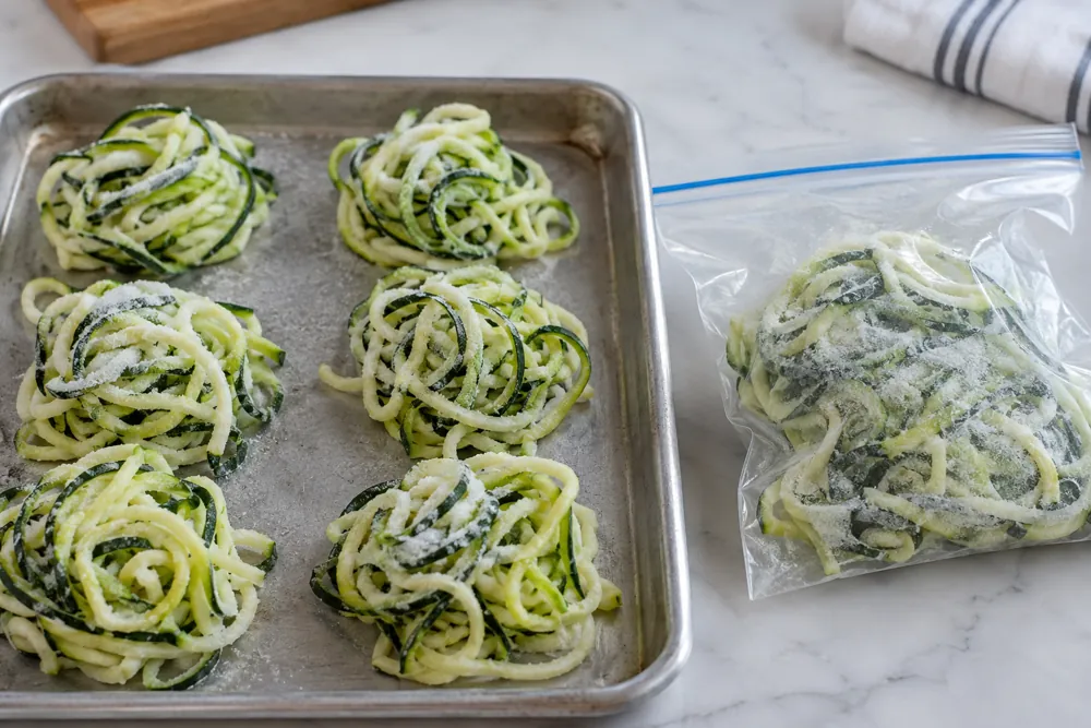 Loose zucchini noodle nests on a tray beside a freezer pouch